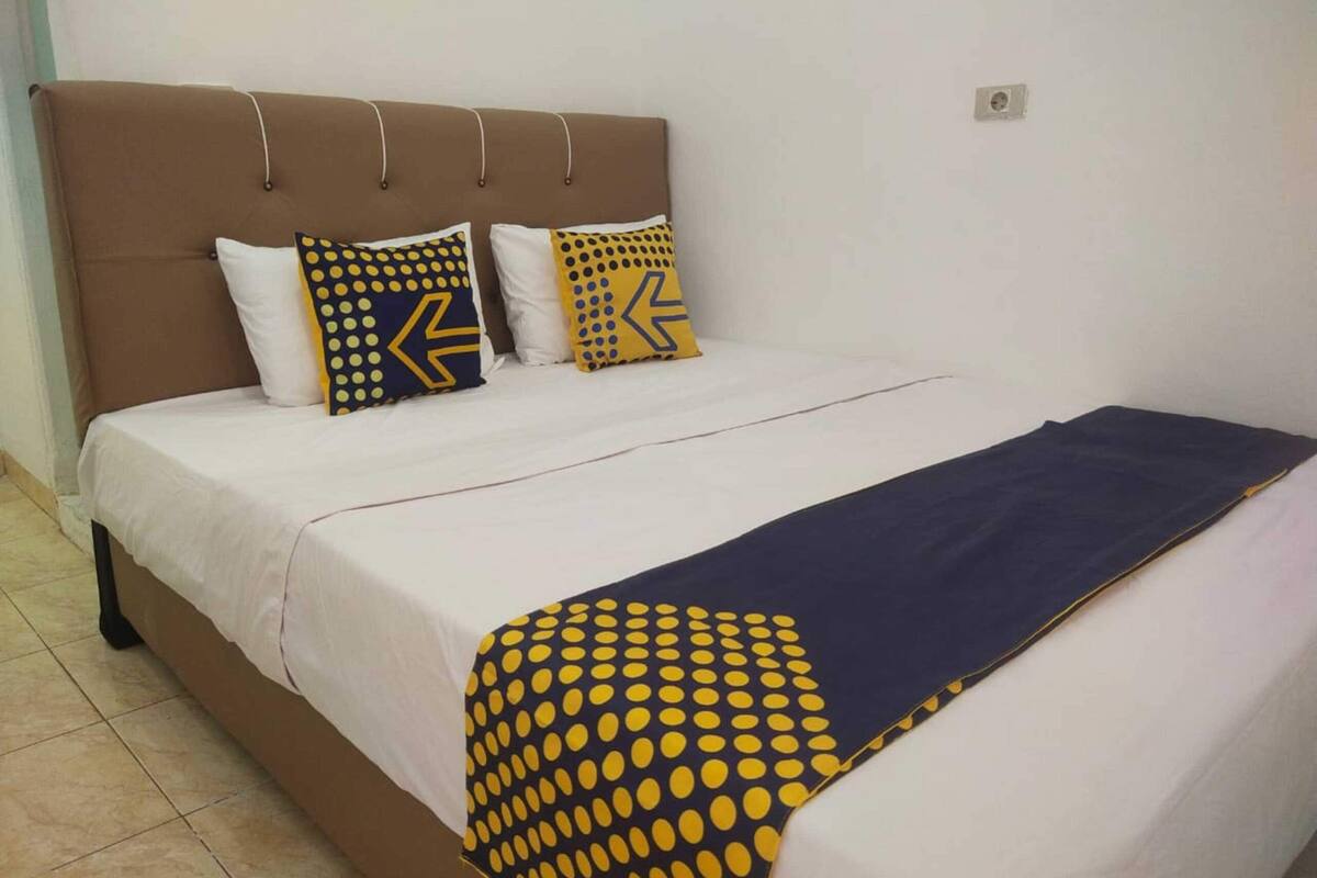 A bed with a white and navy blue bedspread, two pillows with geometric patterns, and a navy blue throw blanket.