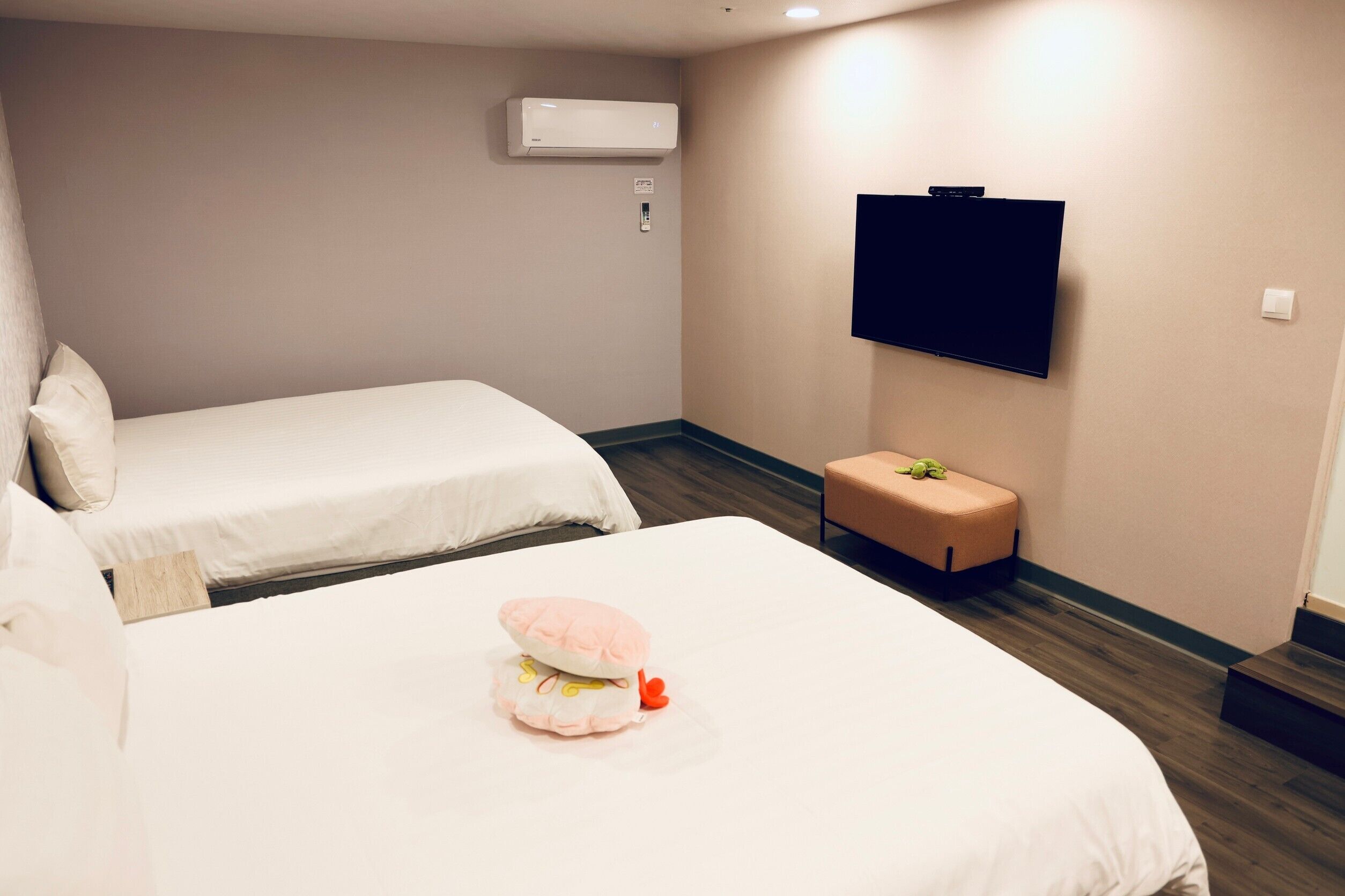 A hotel room with two beds, a television mounted on the wall, and a small seating area.