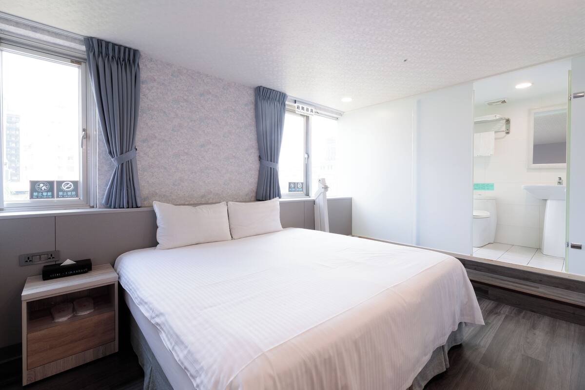 Une chambre d’hôtel moderne avec un grand lit, une table de chevet, un miroir et une vue sur la salle de bain.