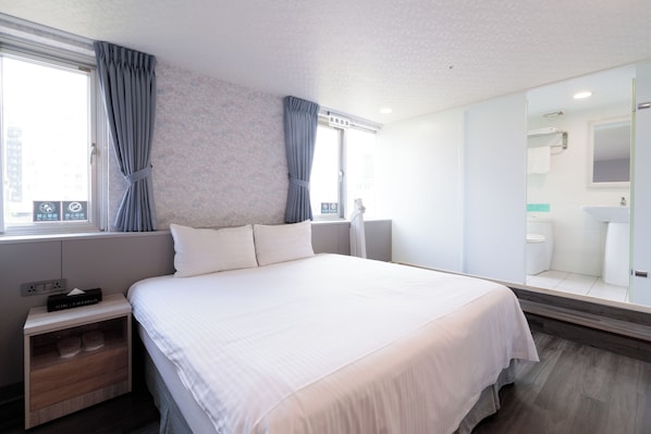 Habitación de hotel moderna con una cama grande, una mesita de noche, un espejo y vistas al baño.