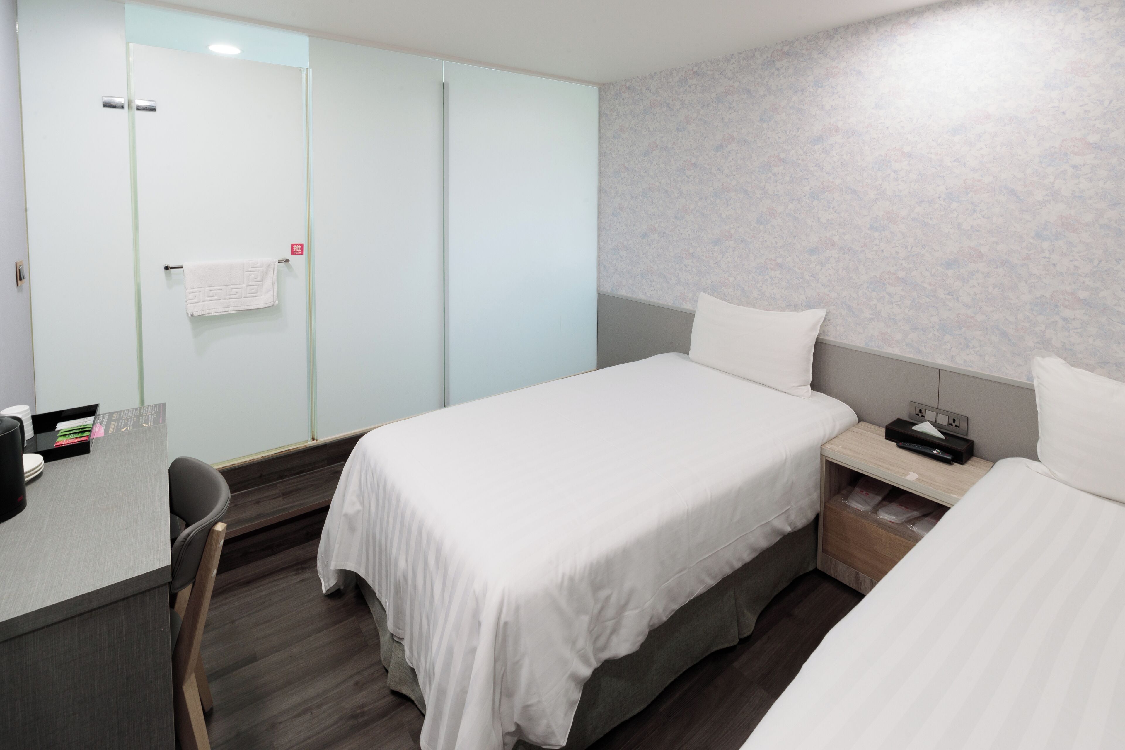 A hotel room with a bed, bedside table, chair, and a desk with a chair.