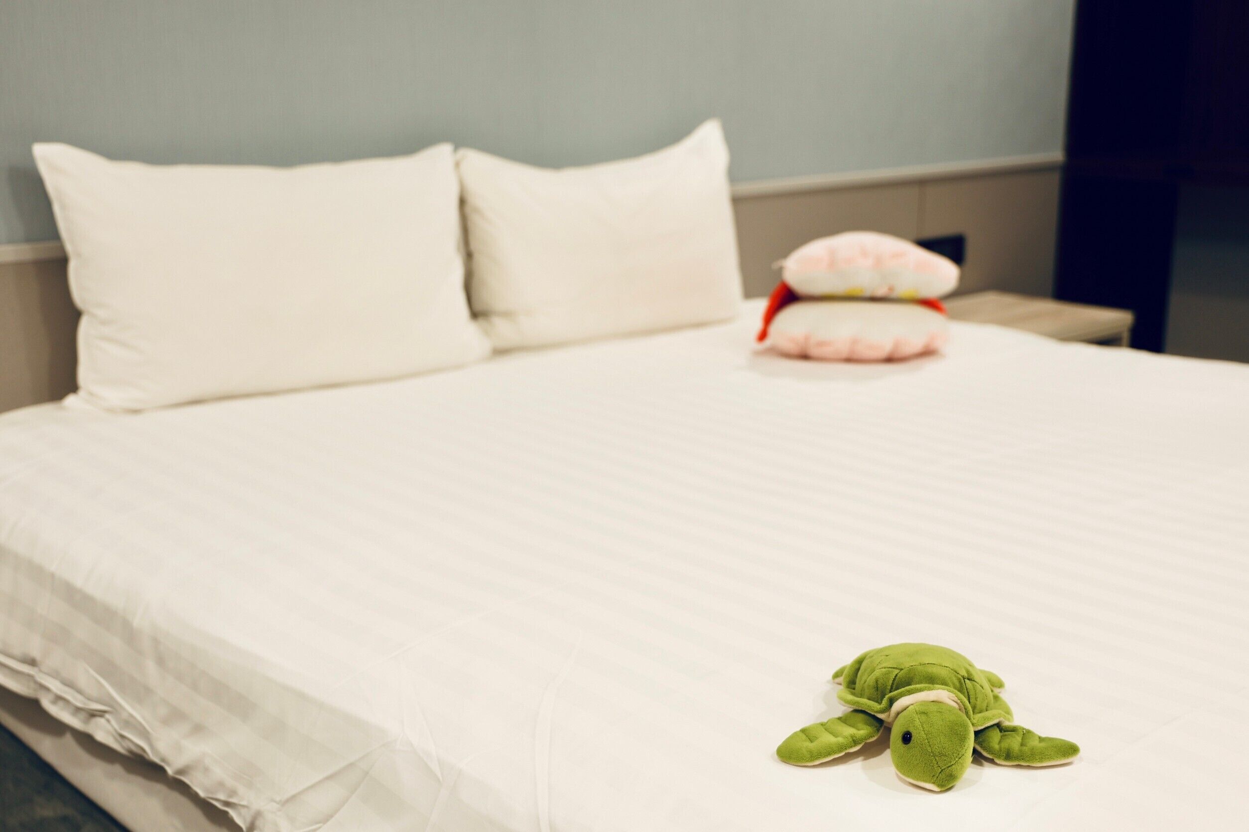 A neatly made bed with white linens and a green plush toy on the bed.