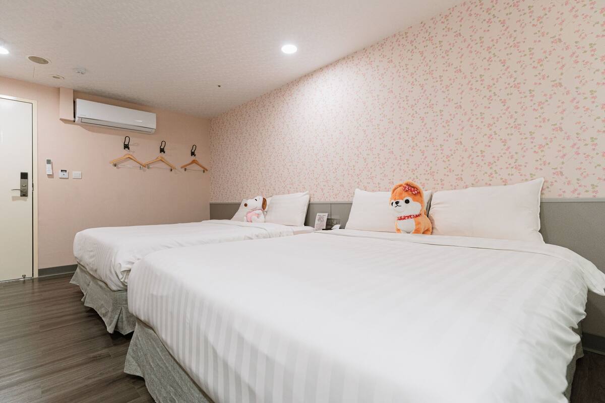 Une chambre d’hôtel avec deux lits, un papier peint à motifs floraux et un climatiseur fixé au mur.
