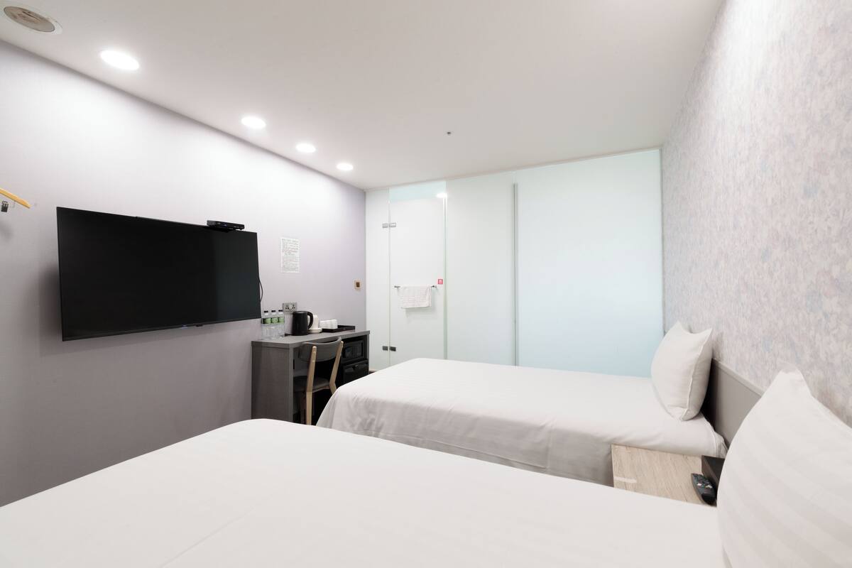 Une chambre d’hôtel moderne équipée de deux lits, d’un téléviseur à écran plat, d’un bureau avec une chaise et d’une petite kitchenette.