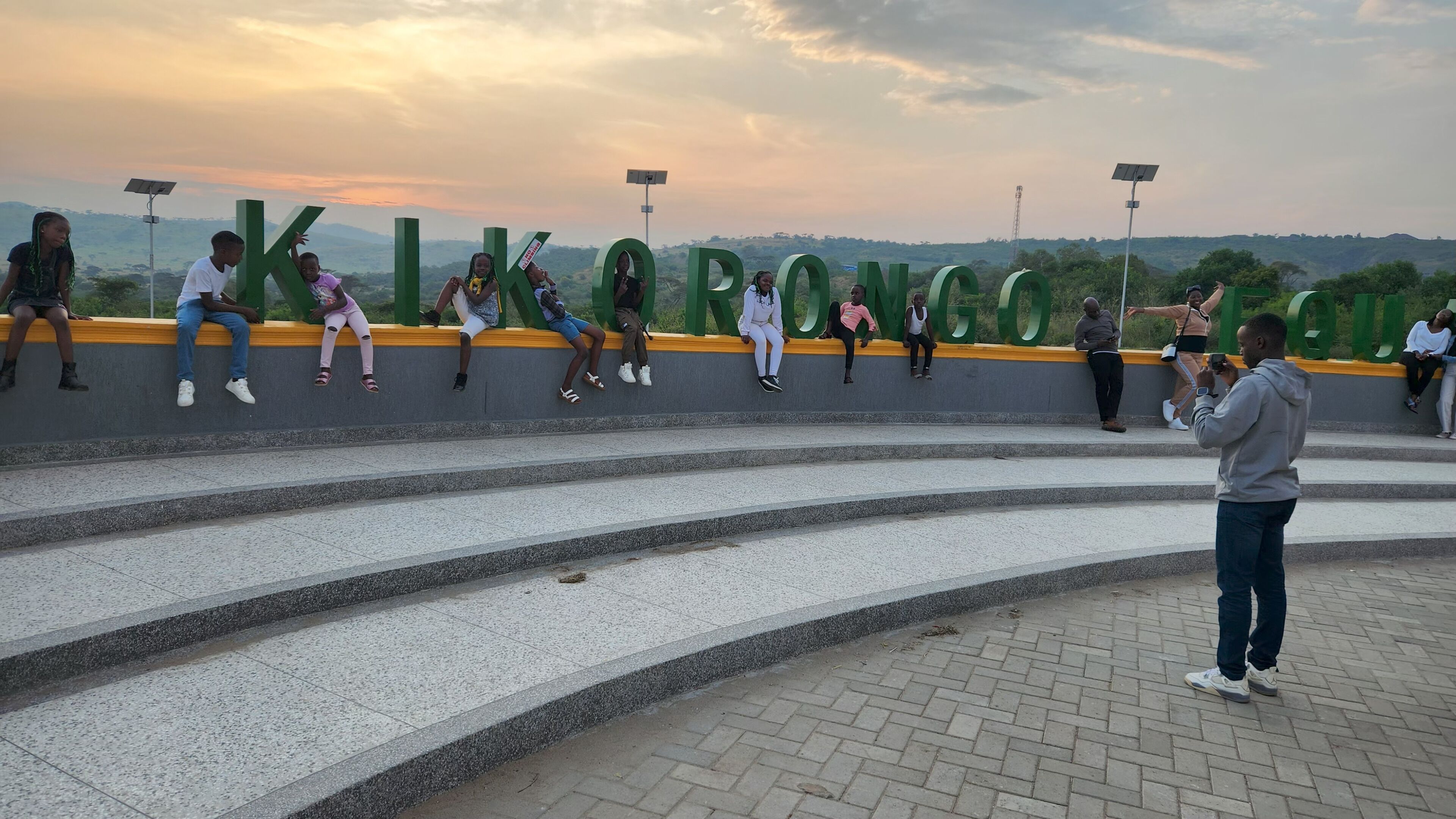 A group of people sitting on a curved wall with large green letters spelling out a location.