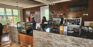 Interior de una cafetería con mostrador, máquinas de café y una variedad de tazas y recipientes en estantes.