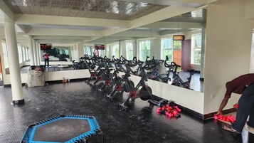 Un gimnasio con bicicletas estáticas, un trampolín y una persona ajustando pesas.