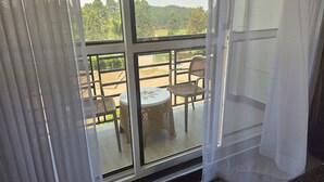 Un balcón con una mesa y sillas, vista a un paisaje verde, y un edificio al fondo.
