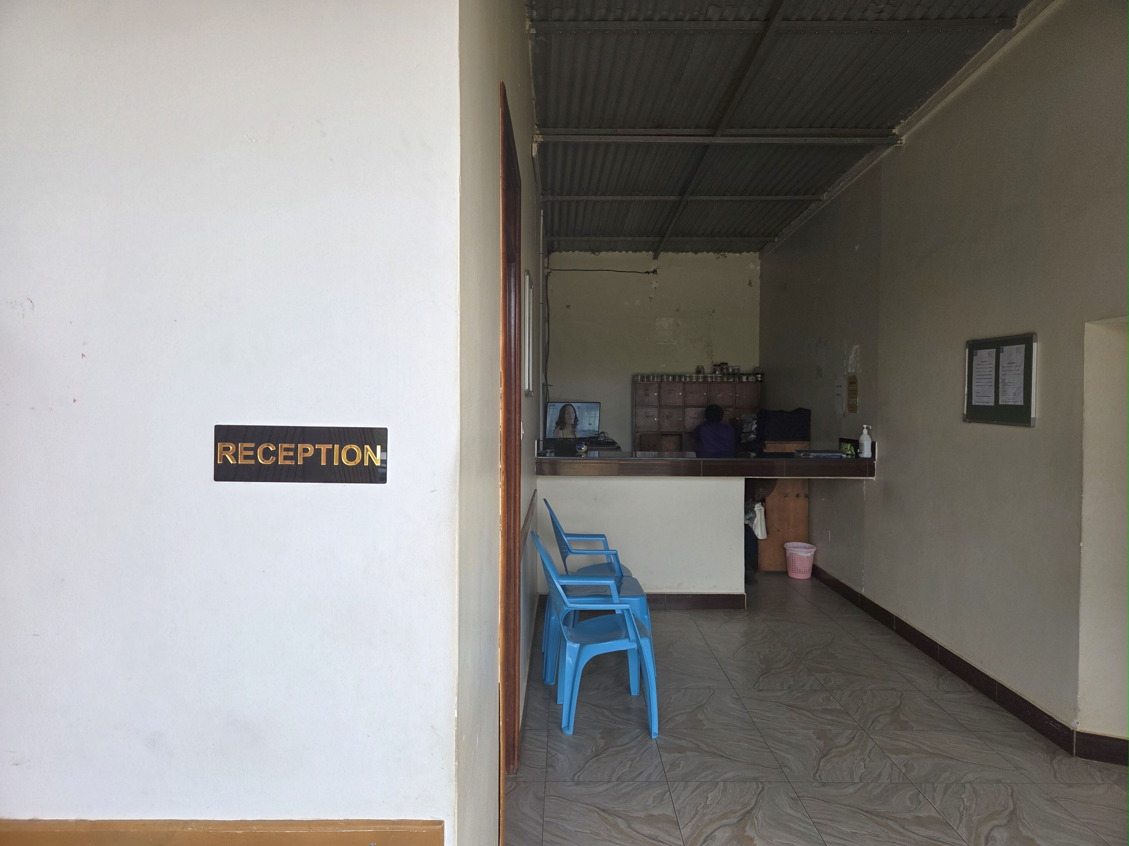 Un área de recepción con un cartel que dice 'RECEPTION', una barra con una computadora y sillas de plástico azules.