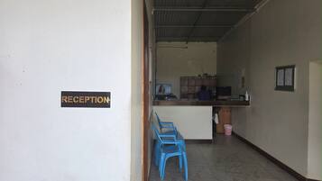 Un área de recepción con un cartel que dice 'RECEPTION', una barra con una computadora y sillas de plástico azules.