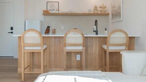 A modern kitchen with wooden chairs, a white countertop, and a hanging light fixture.