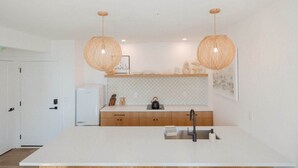A modern kitchen with a large island, two pendant lights, and a white refrigerator.
