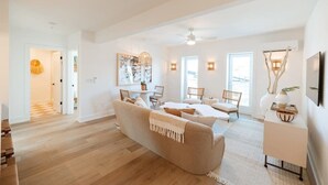 Ein großzügiges Wohnzimmer mit einem großen beigen Sofa, einem Essbereich mit Tisch und Stühlen sowie einem weißen Konsolentisch mit Dekorationselementen.
