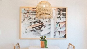 Ein Zimmer mit einem runden Tisch, zwei Korbstühlen, einer Hängeleuchte und einem großen abstrakten Gemälde an der Wand.