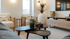 Una sala de estar moderna con un sof á, sillones, una mesa de centro, una planta grande, un televisor y un aparador.