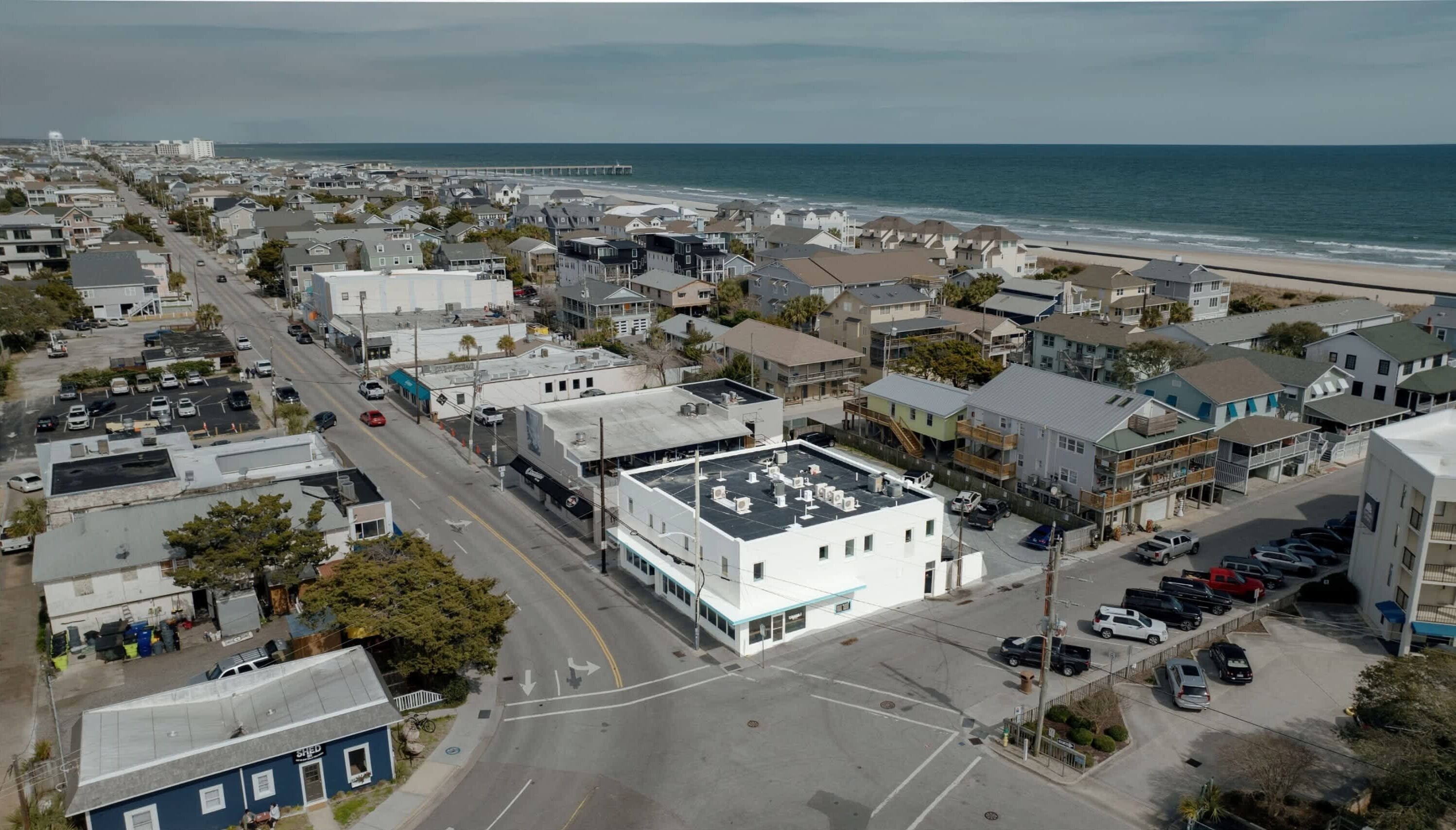 An aerial view of a coastal town with a beach, houses, and a road leading to the beach.