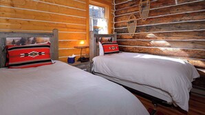 A log cabin room with two beds, a window, and a wall-mounted basket. - "Wild Iris" Historic Home in downtown CB, Dog Friendly! (Crested Butte)