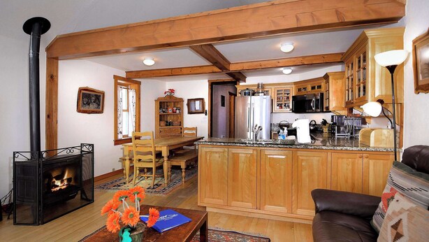 A cozy living room with a fireplace, wooden furniture, and a kitchen area with wooden cabinets and appliances. - "Wild Iris" Historic Home in downtown CB, Dog Friendly! (Crested Butte)