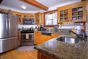 A kitchen with wooden cabinets, stainless steel appliances, granite countertops, and a window with curtains. - "Wild Iris" Historic Home in downtown CB, Dog Friendly! (Crested Butte)