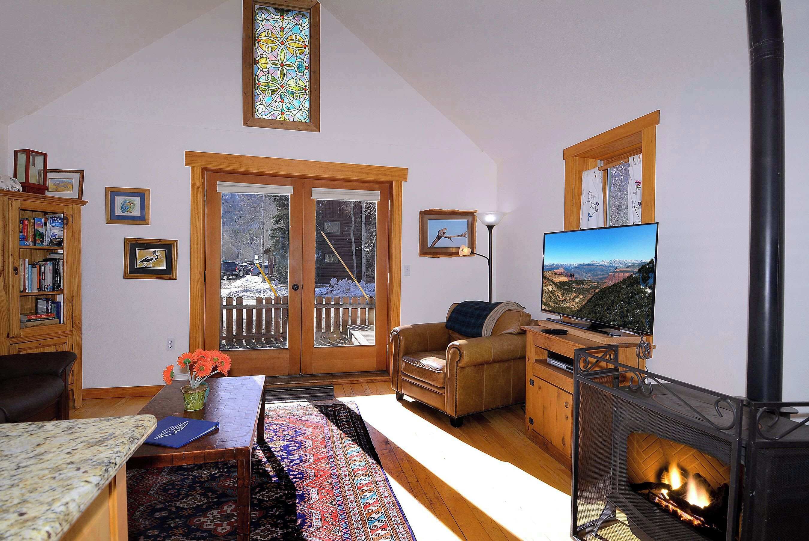 A cozy living room with a fireplace, a television, and a view through the glass doors.