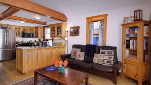 A cozy living room with a leather sofa, wooden bookshelves, and a kitchen area with wooden cabinets and modern appliances. - "Wild Iris" Historic Home in downtown CB, Dog Friendly! (Crested Butte)