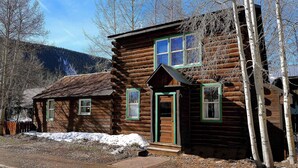 A rustic log cabin with a front porch, a small attached shed, and a mountain backdrop. - "Wild Iris" Historic Home in downtown CB, Dog Friendly! (Crested Butte)