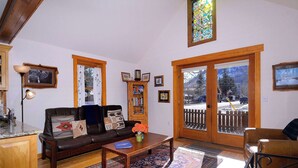 A living room with a leather sofa, a coffee table, a bookshelf, and a large window with a view of a snowy landscape. - "Wild Iris" Historic Home in downtown CB, Dog Friendly! (Crested Butte)