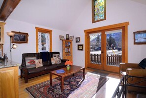 A living room with a leather sofa, a coffee table, a bookshelf, and a large window with a view of a snowy landscape. - "Wild Iris" Historic Home in downtown CB, Dog Friendly! (Crested Butte)