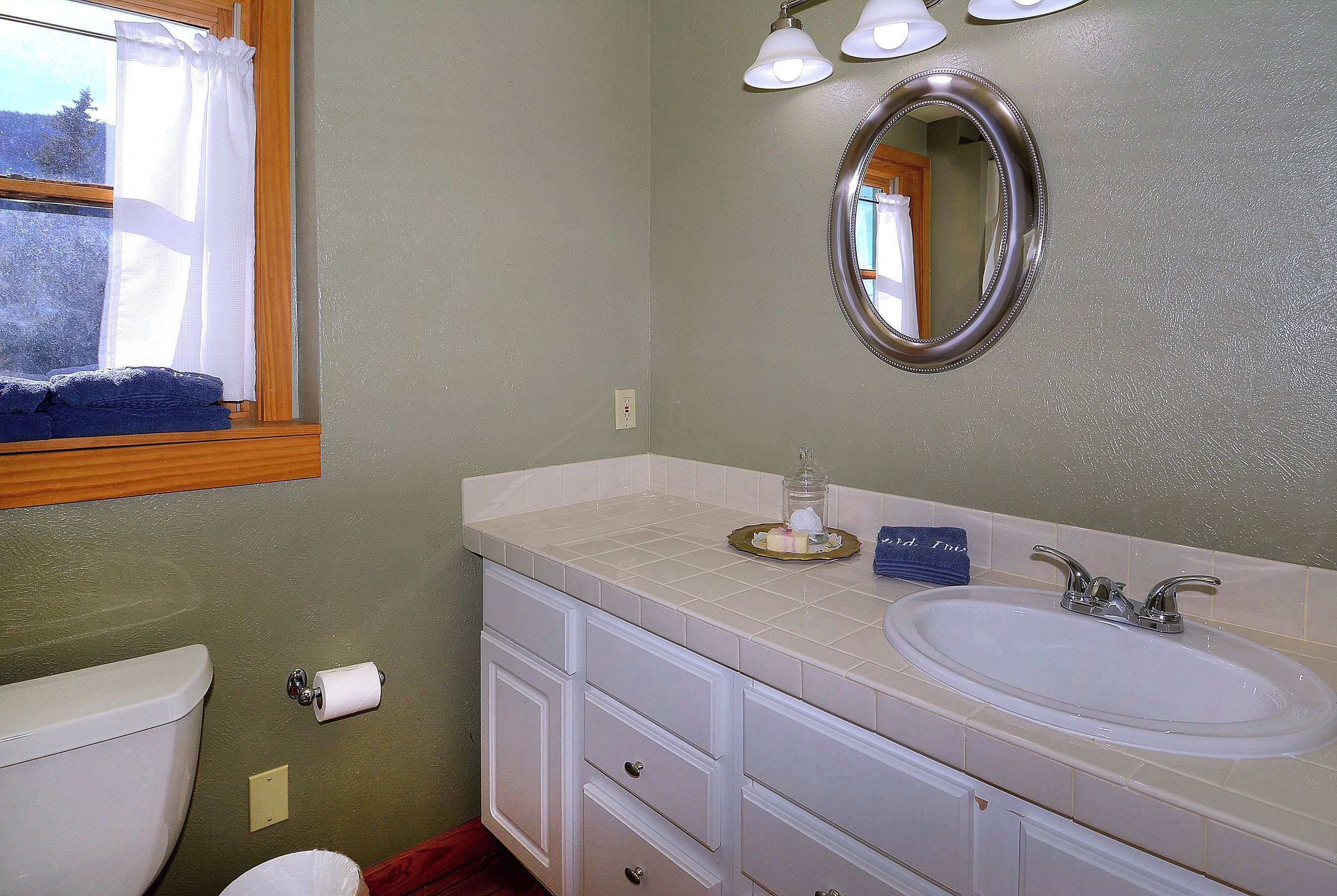 A bathroom with a toilet, sink, vanity, and a window with a view of trees.