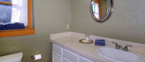 A bathroom with a toilet, sink, vanity, and a window with a view of trees.