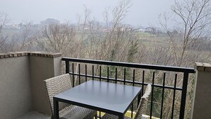 A balcony with a table and chairs, a tiled floor, and a view of a rural landscape. - GiardinidiEva (San Floriano del Collio)