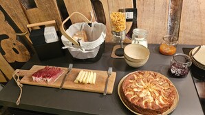 A breakfast table with various food items, including a wooden cutting board with cheese and meat, a round apple tart, and a basket with bread. - GiardinidiEva (San Floriano del Collio)