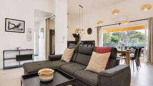 Un salon moderne avec un canapé d’angle gris, une table basse noire et un coin repas comprenant une table et des chaises en bois.