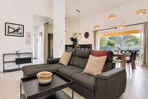 Una sala de estar moderna con un sofá seccional gris, una mesa de centro negra y un comedor con una mesa y sillas de madera.