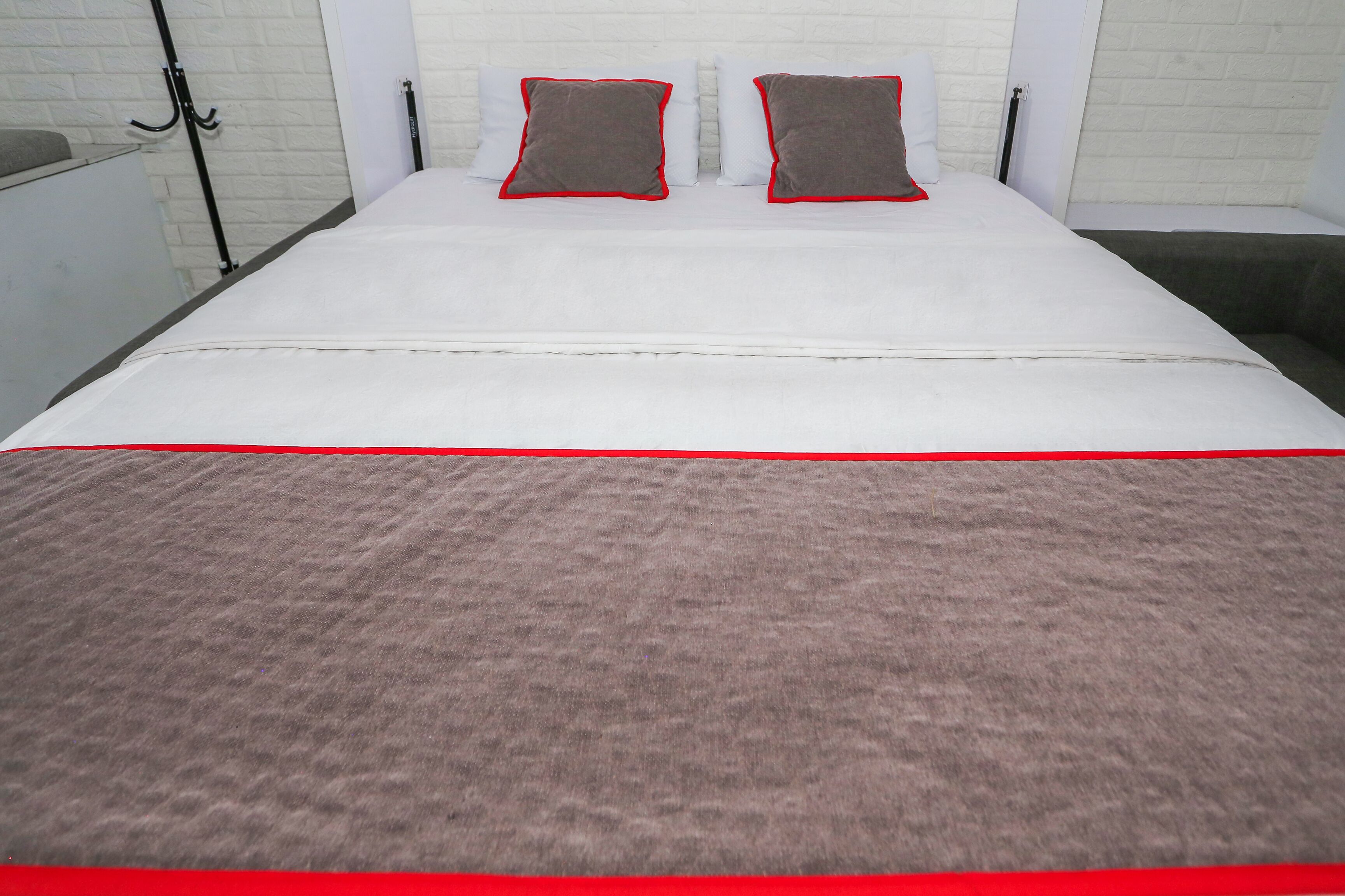 Ein Bett mit einer weißen Matratze, zwei Kissen mit roter Bordüre und einer braunen Decke.