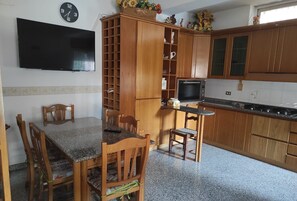 Una cocina con armarios de madera, un microondas, un televisor y una mesa de comedor con sillas.