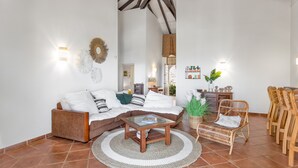 Una sala de estar con un sofá marrón, una mesa de centro de vidrio y una silla de mimbre.
