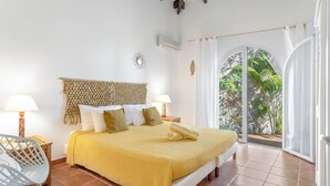 Un dormitorio con cama, dos mesitas de noche con lámparas, una silla y vistas a la vegetación a través de un ventanal.