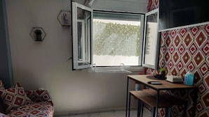 Quarto pequeno e bem iluminado, com uma cama, uma mesa e uma janela.