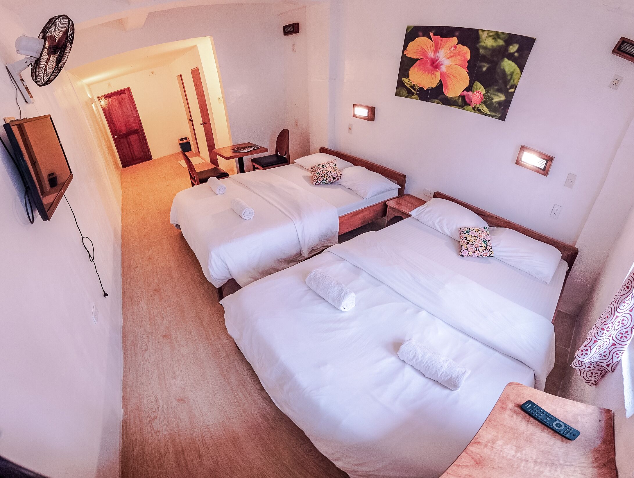 Camera d'albergo con due letti, una scrivania, una sedia, una ventola, un quadro e un telecomando.