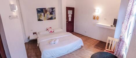 A bedroom with a bed, a desk, a chair, a ceiling fan, and a door.
