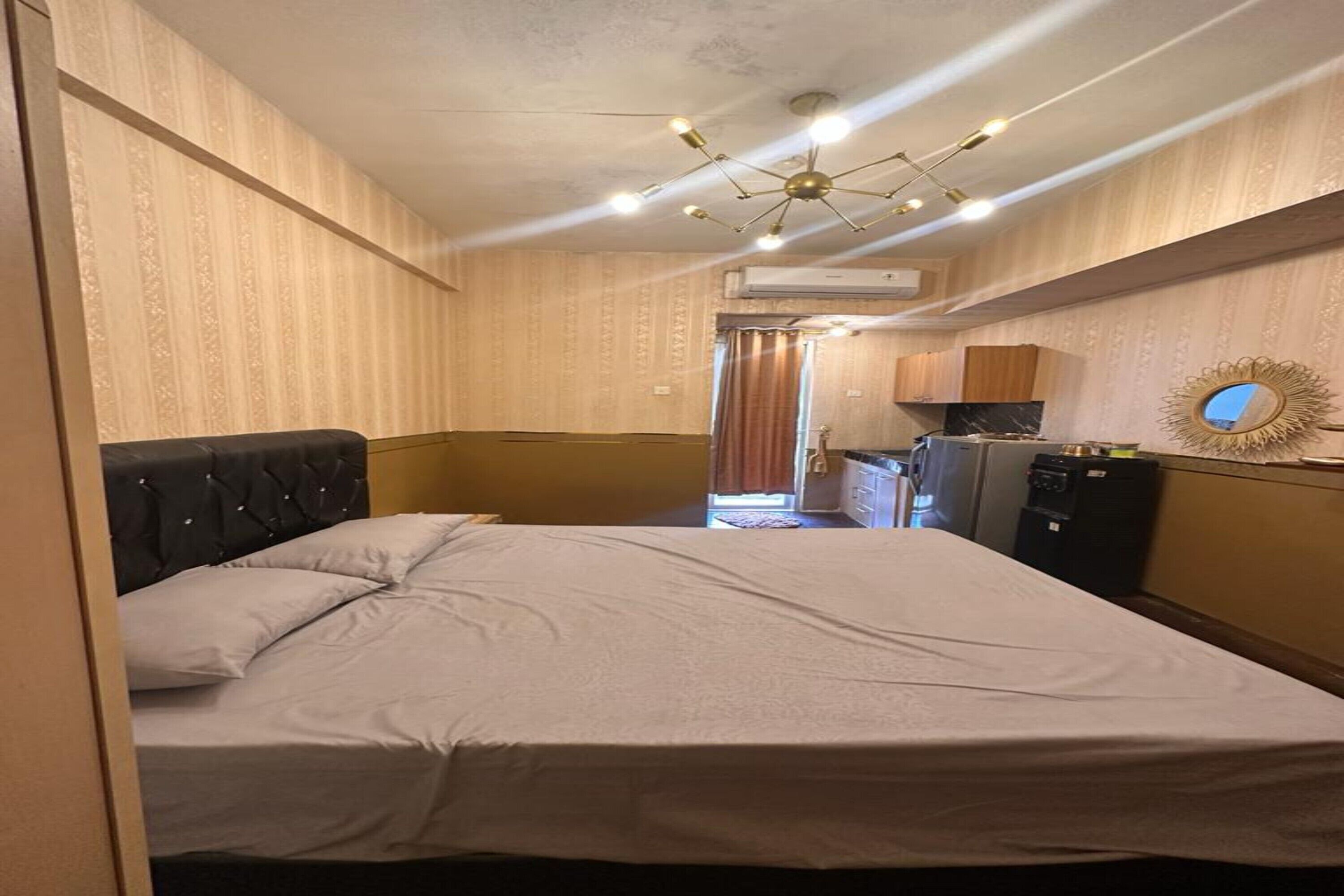 A hotel room with a bed, a small kitchenette, and a bathroom visible in the background.