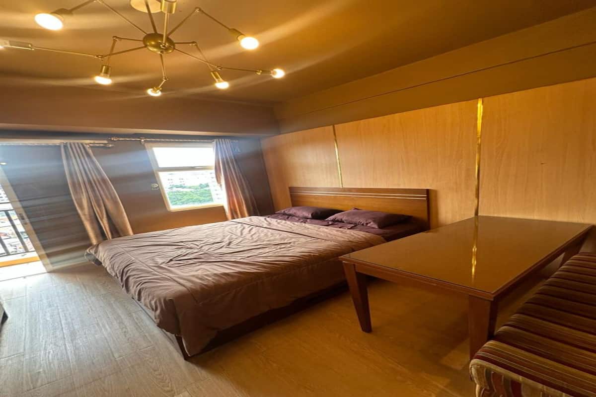 A bedroom with a bed, a wooden table, and a view of the outdoors through a window.