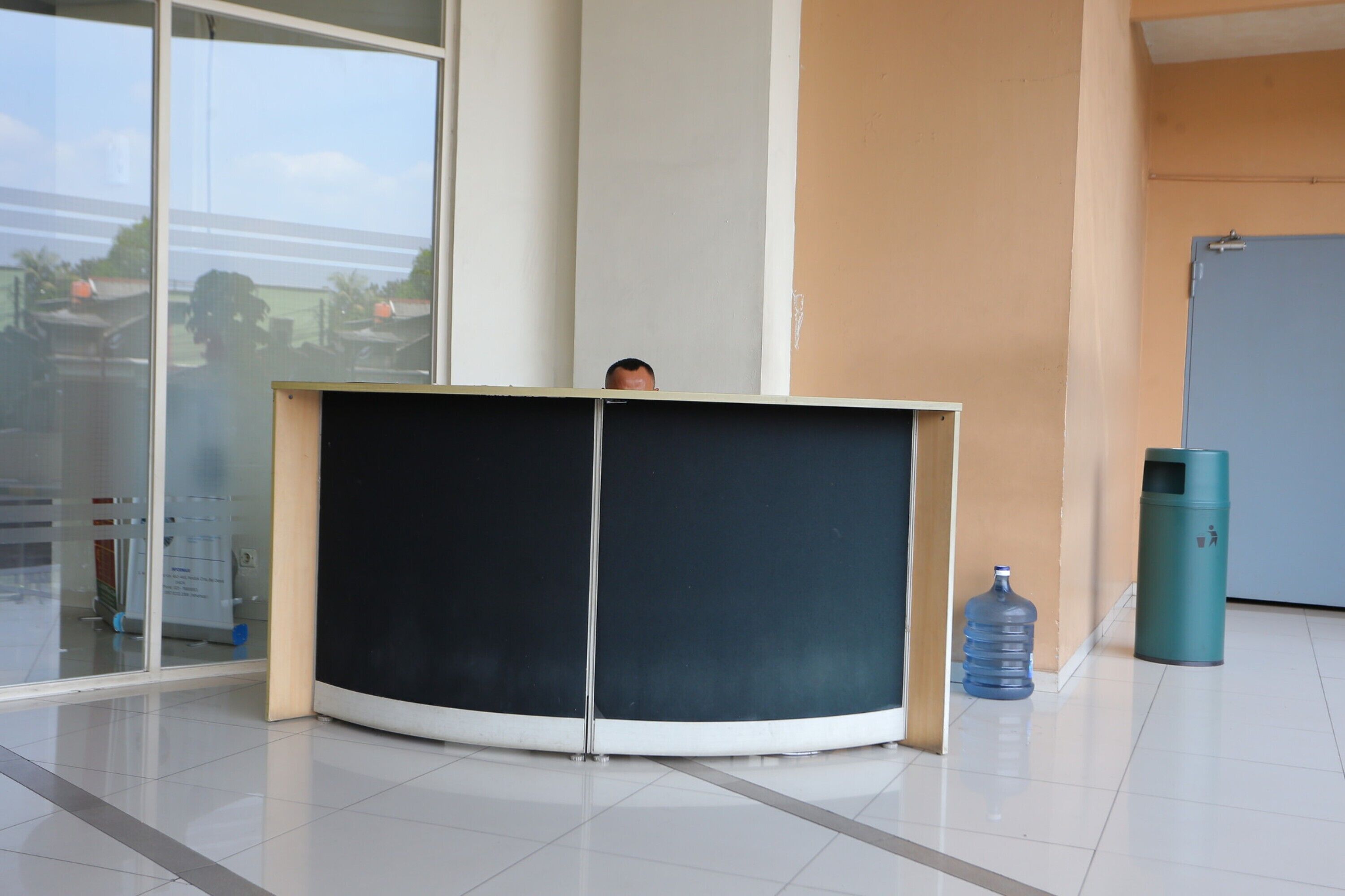 A reception desk in a modern building with a glass door, a water dispenser, and a trash bin.