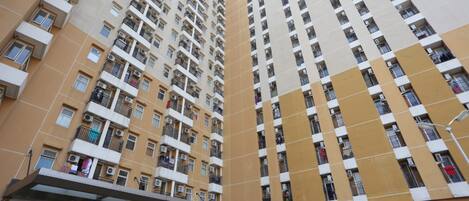 Um edifício residencial alto, com várias varandas, aparelhos de ar condicionado e uma loja no andar térreo.