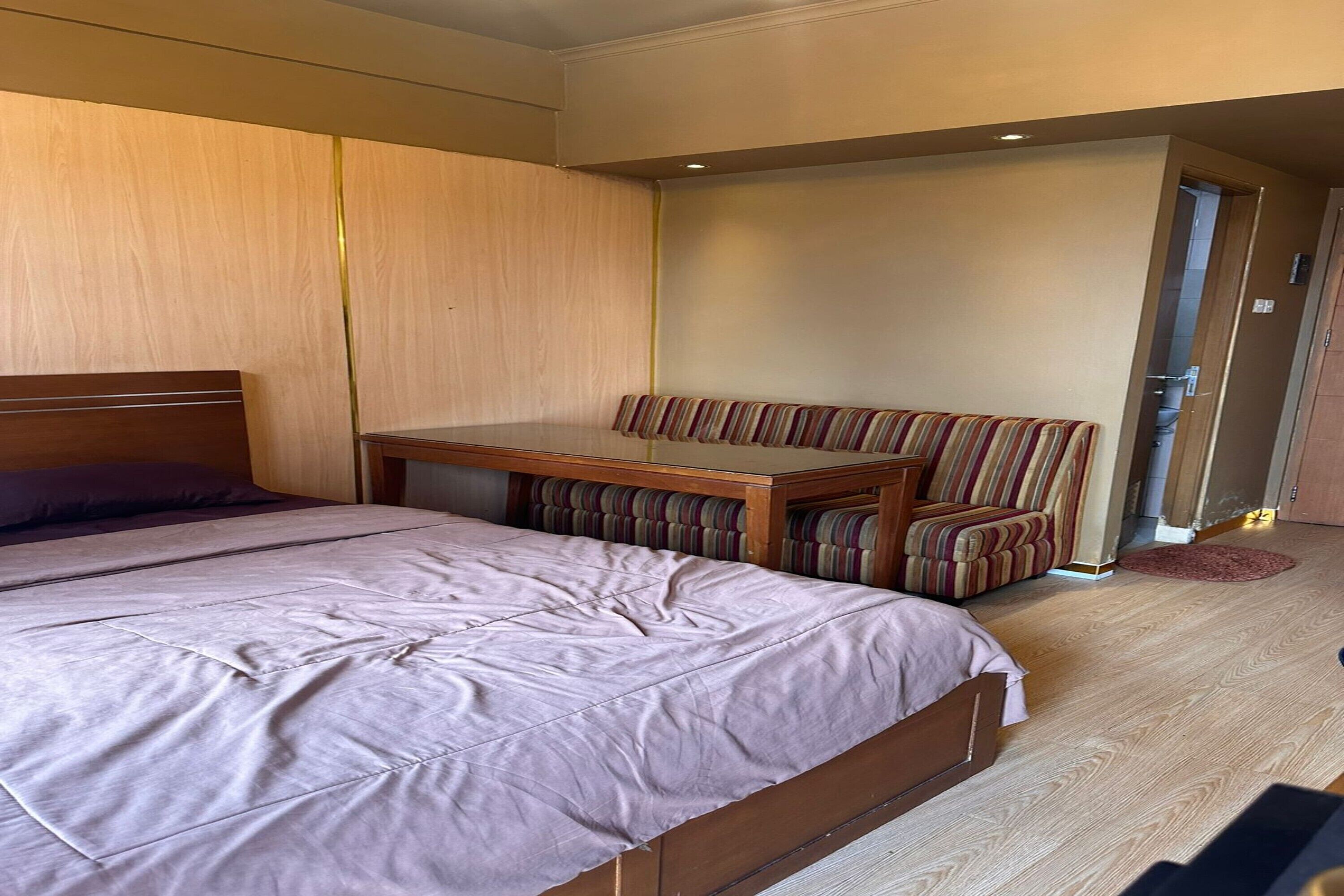 Een slaapkamer met een bed, een houten tafel en een gestreept bankje.