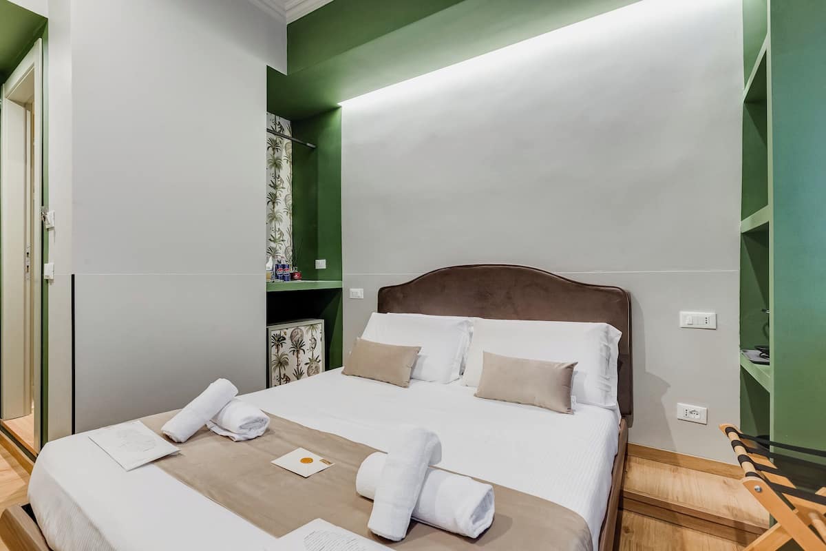 A neatly made bed with white linens and two rolled towels, a wooden headboard, and a green accent wall.