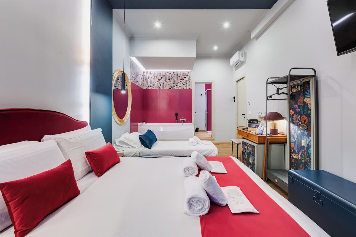A modern hotel room with a large bed, a small desk, a vanity, and a shower area.