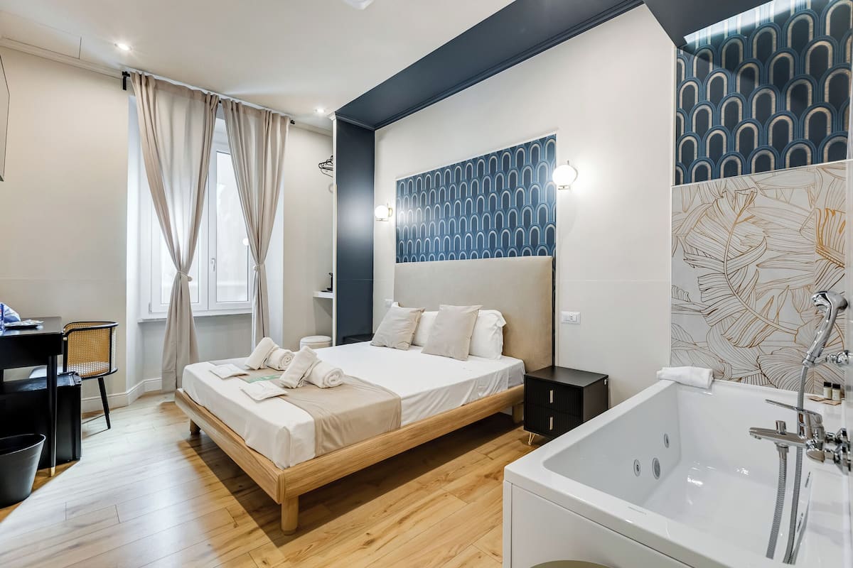 A modern bedroom with a wooden bed, a large window with curtains, a wall-mounted light fixture, and a bathroom with a bathtub.