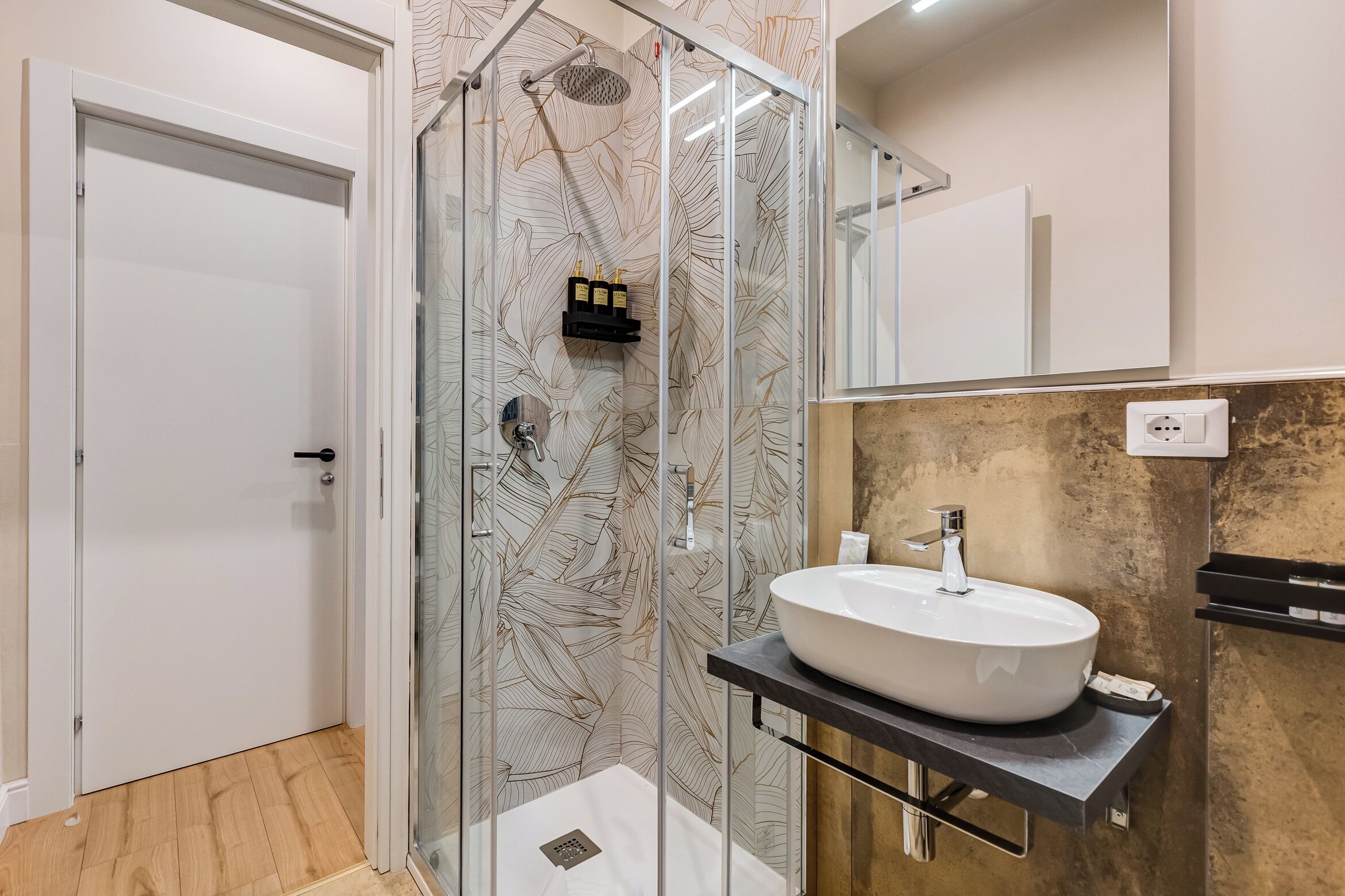A modern bathroom with a glass shower enclosure, a white sink, and a wooden floor.